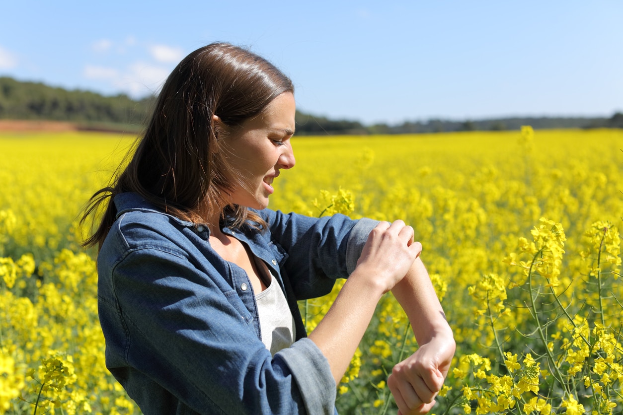 A woman standing outside reacts to being stung by an unseen insect.